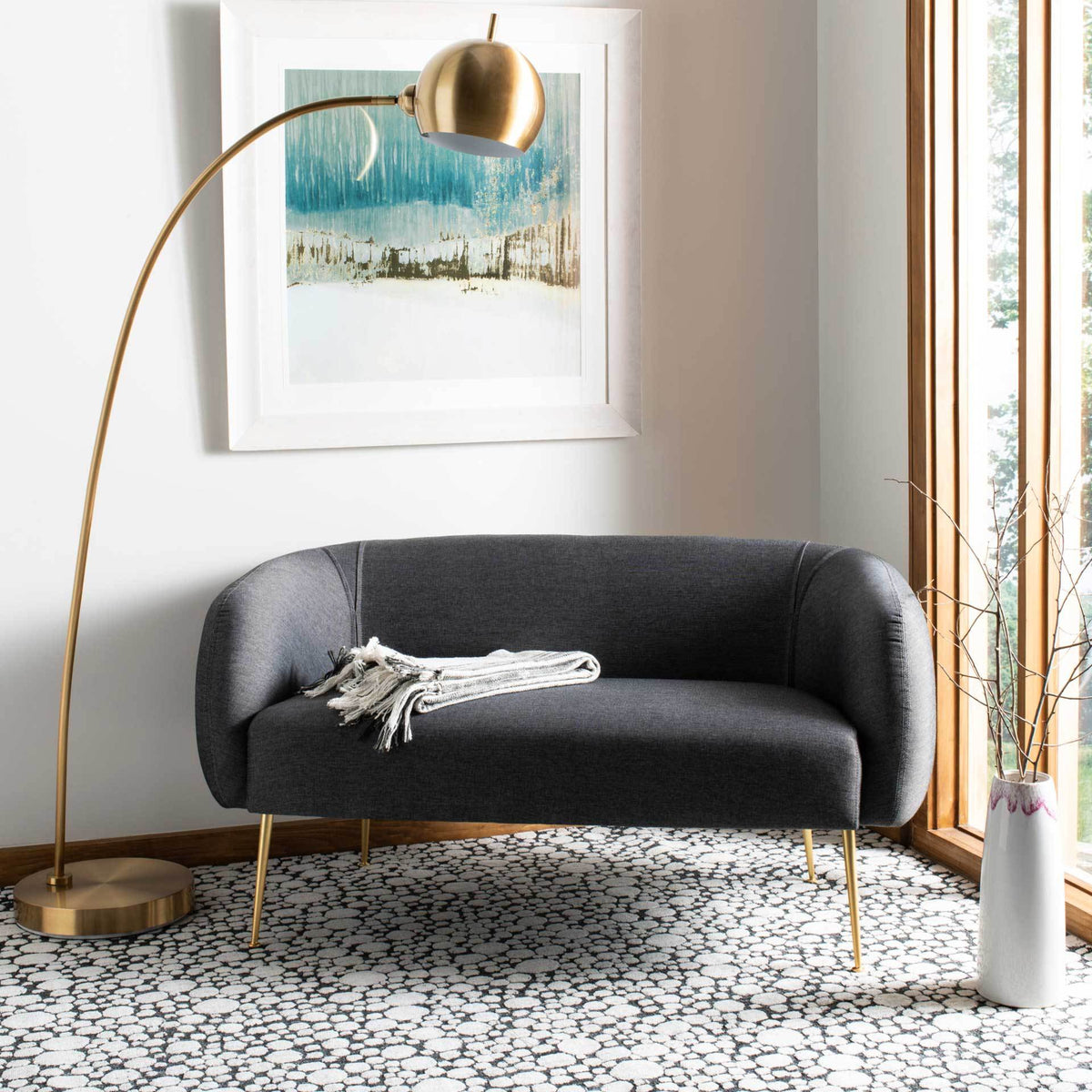 A softly curved gray loveseat brings an inviting cushioned seat and gold-tone accents to the living space.