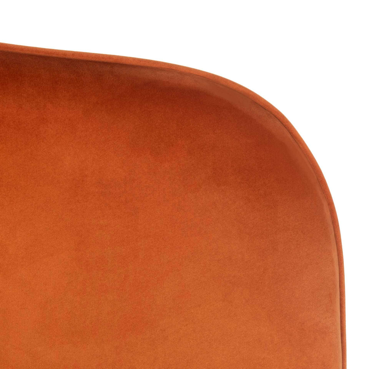 Fine piping traces the rounded edge of the chair's soft sienna velvet upholstery