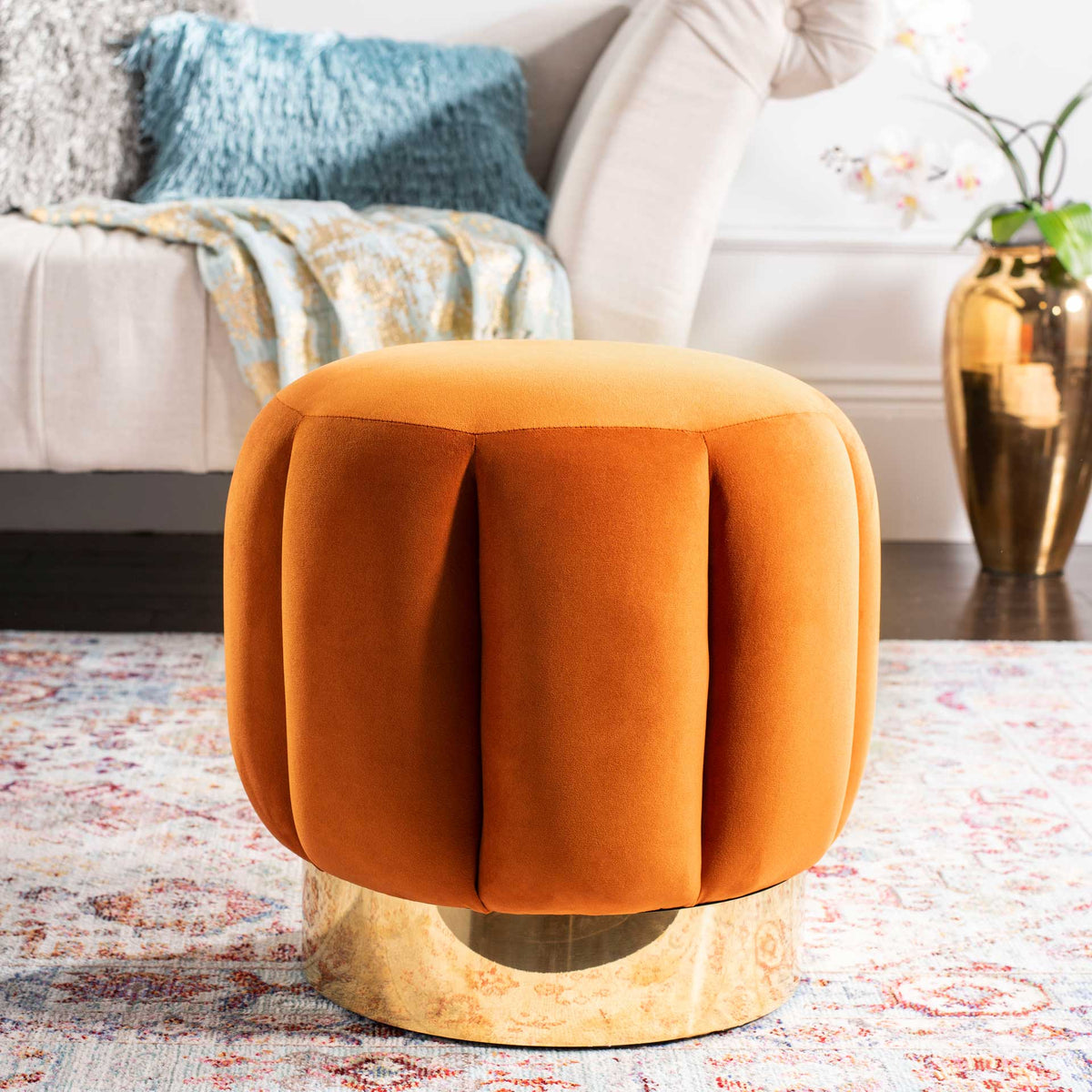 A sienna velvet ottoman warms the living room with sculpted upholstery and a gold base.