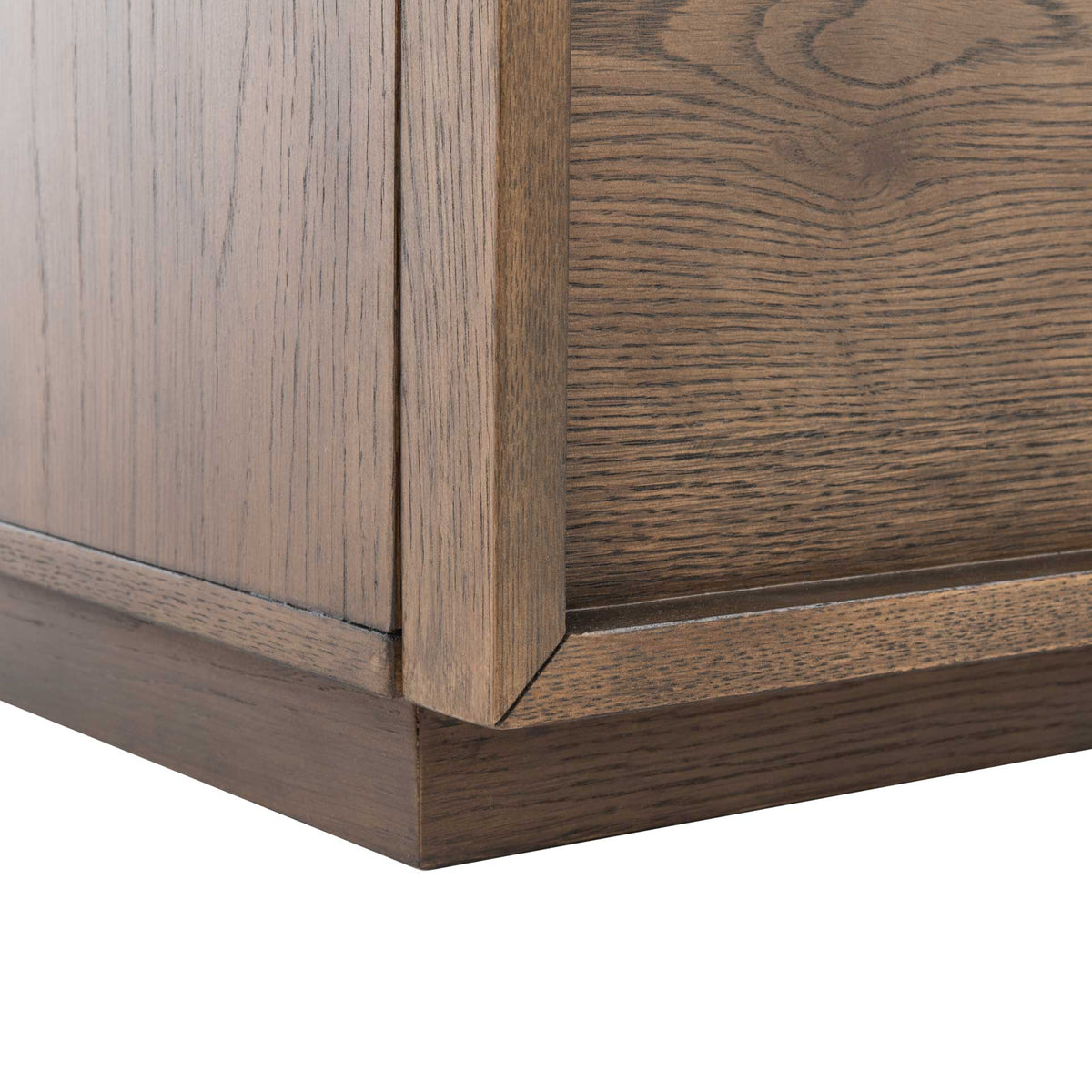 A low plinth base anchors the framed lower drawer and its rich oak grain.