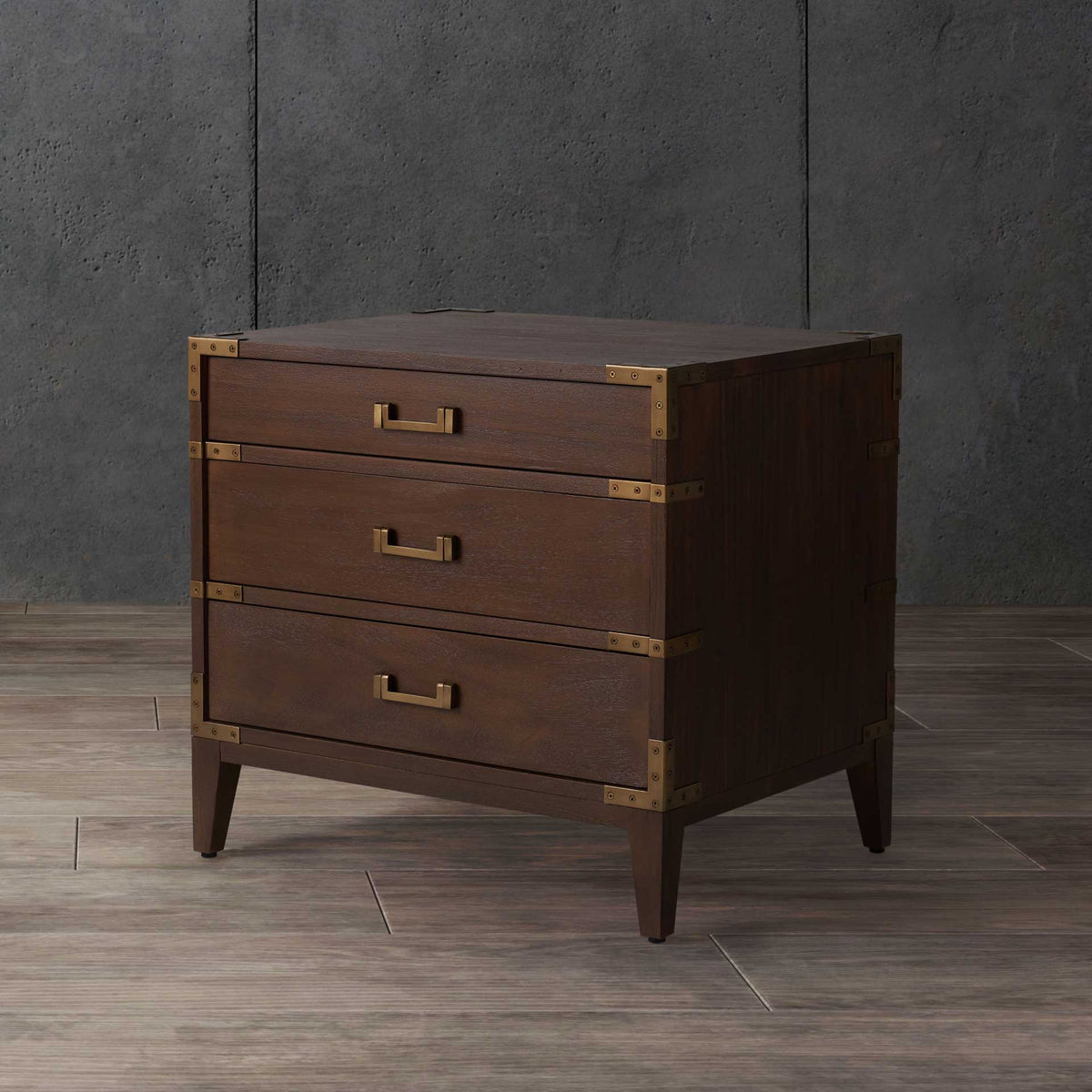 Dark brown wood and brass-tone accents give this three-drawer nightstand a vintage trunk feel