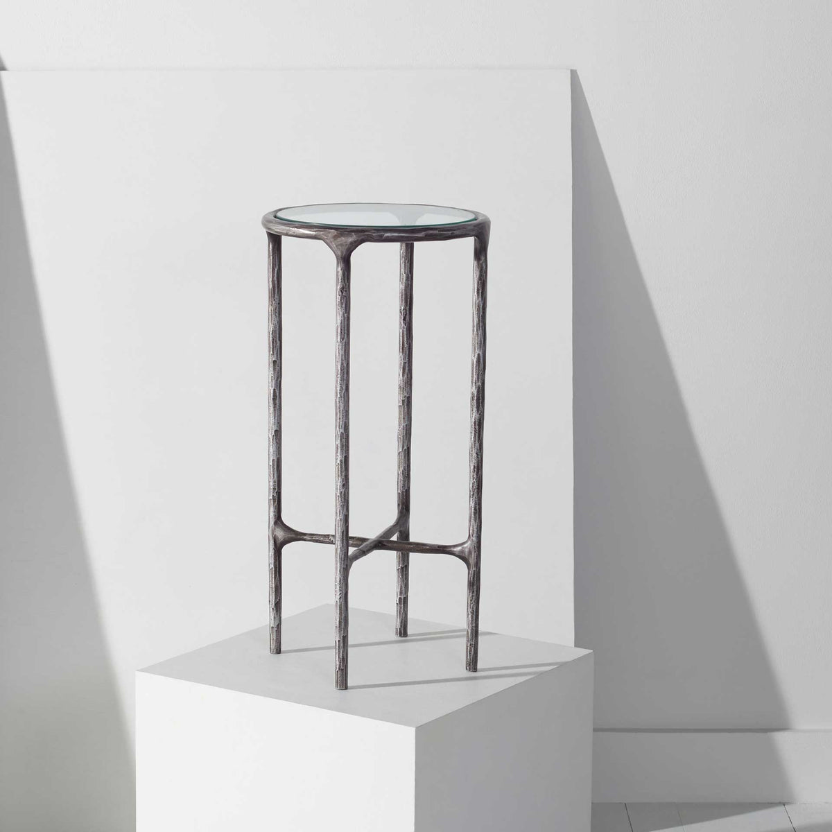 A tall, open silver-toned frame and petite glass top lend an airy feel to this end table.