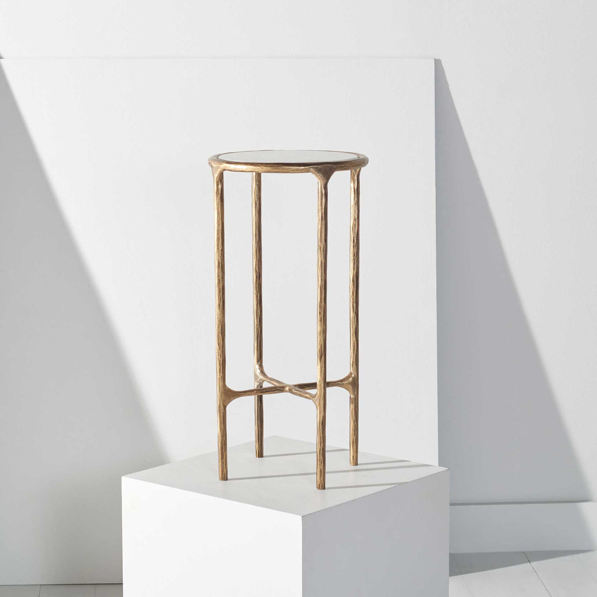 A tall, open brass-toned frame lifts the petite marble top for an elegant accent.