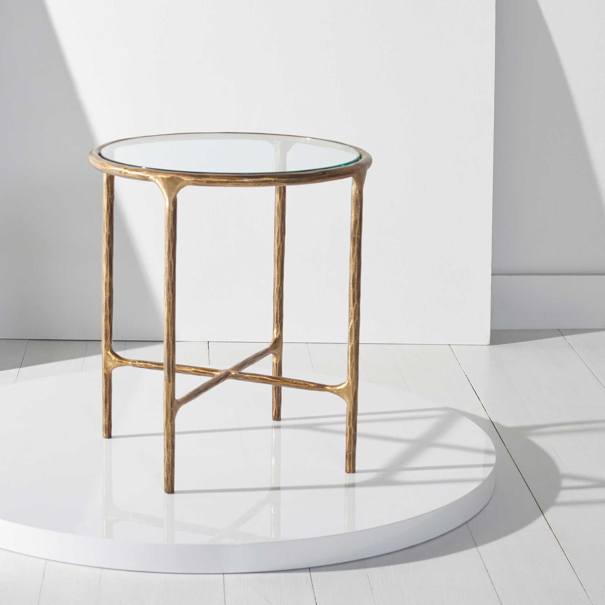 The clear round top and warm metallic frame create an airy accent with sculptural crossed supports.