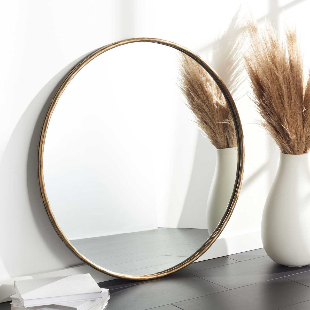 A large round mirror in a warm brass-finish frame adds depth and light to a room