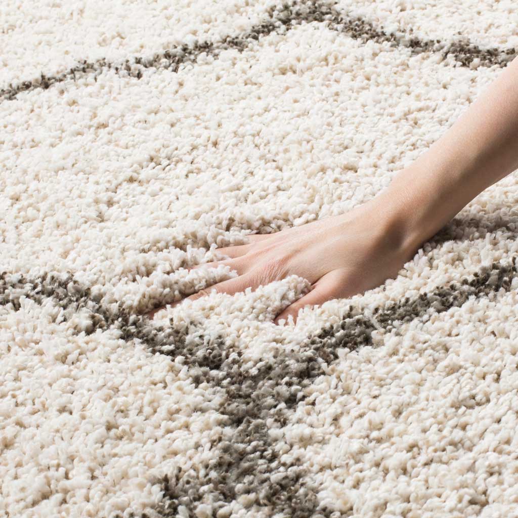 A hand presses into plush ivory pile beside a gray contour