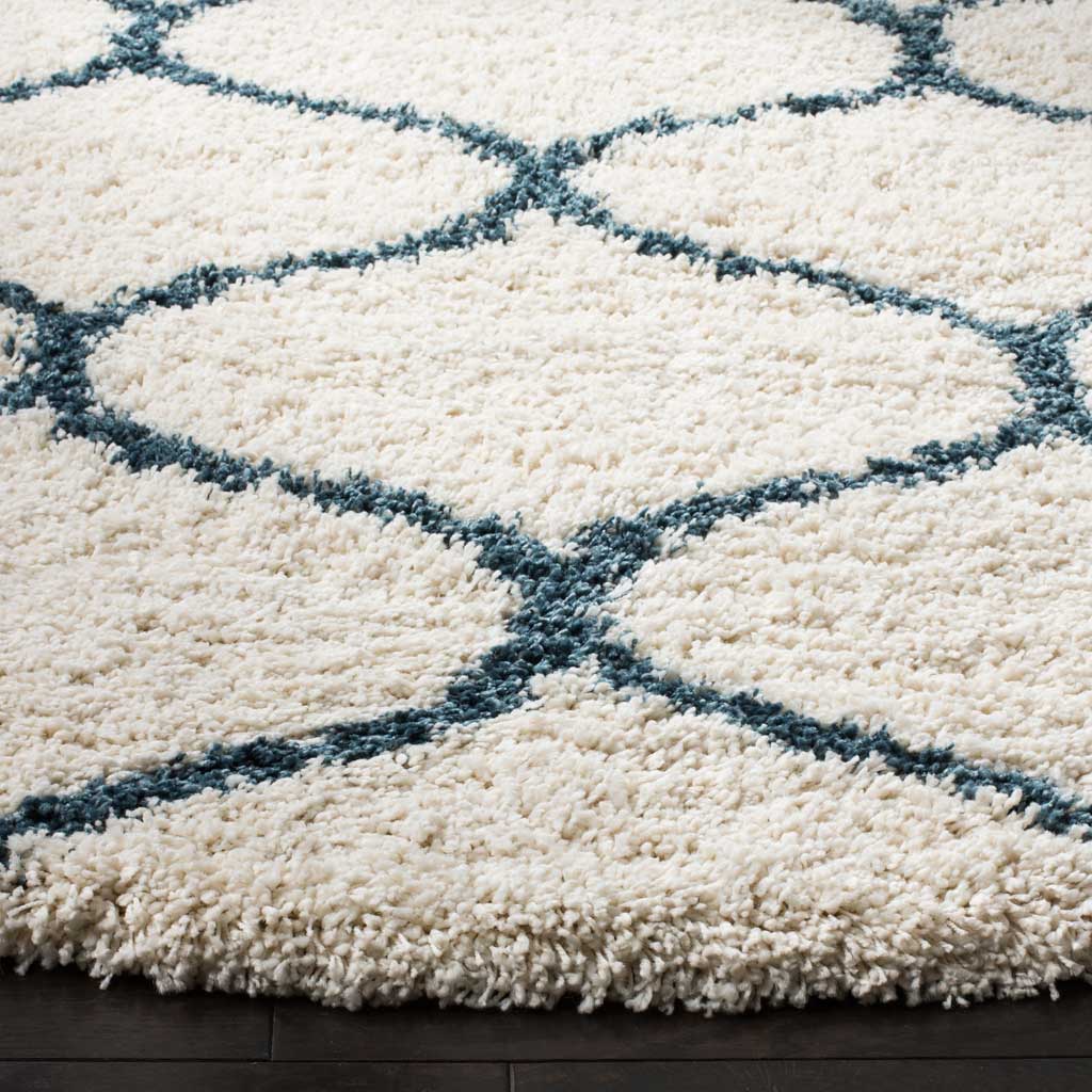 Raised steel blue lines cross thick ivory shag near the rug's cushioned edge