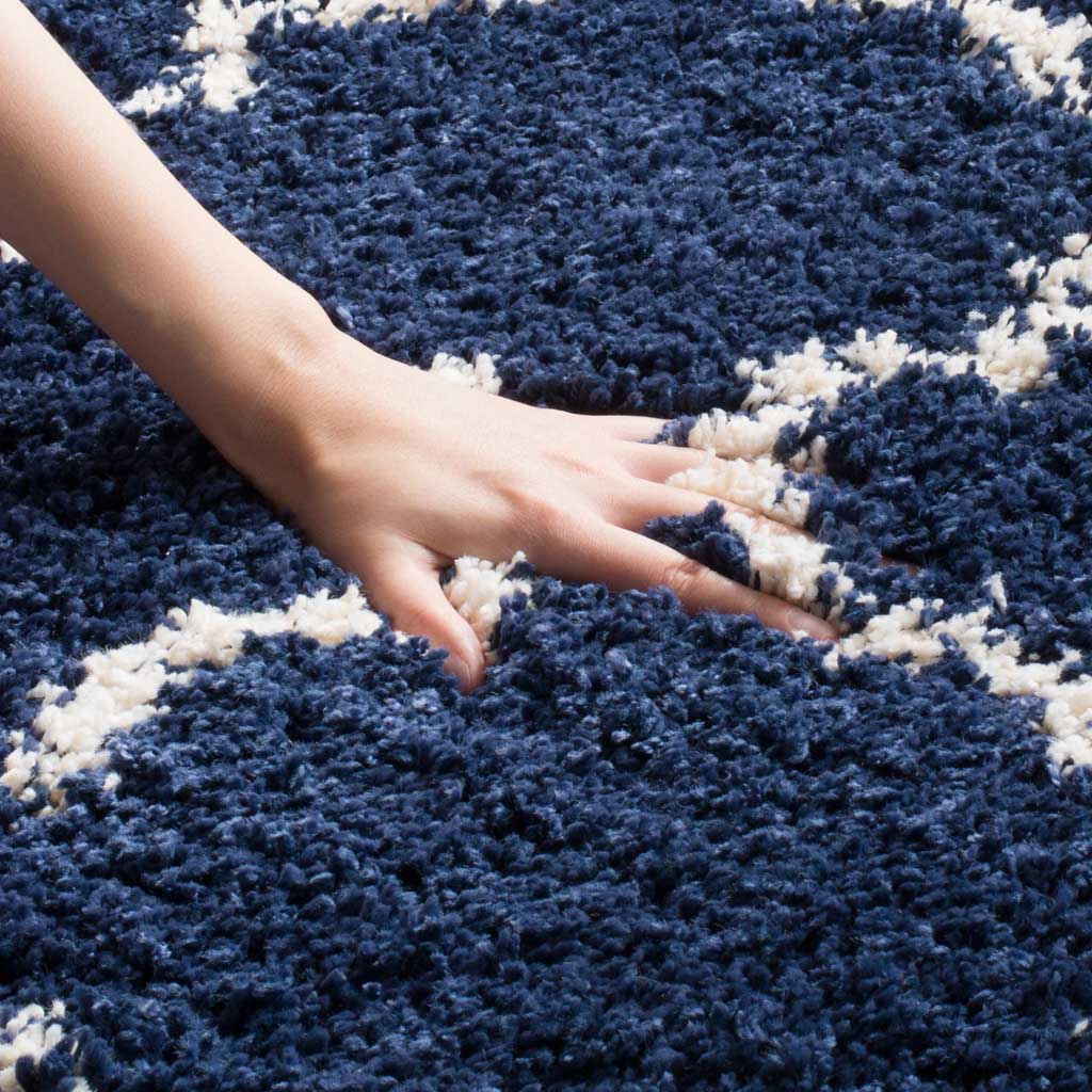A hand sinks into the navy pile beside an ivory quatrefoil line