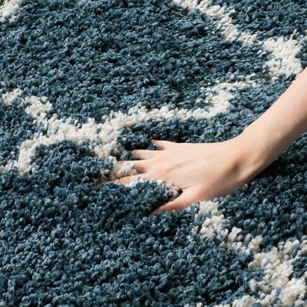 A hand sinks into the dense slate blue shag beside ivory lines