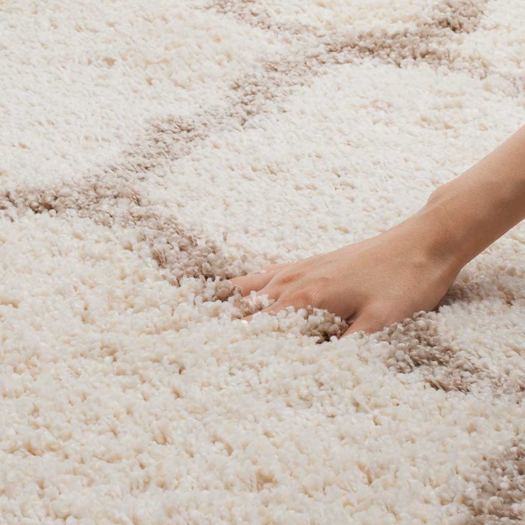 A hand presses into the lofty ivory pile beside a beige line