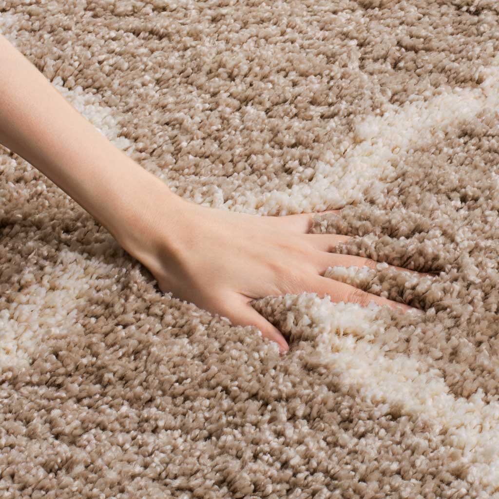 A hand presses into deep beige shag beside an ivory line