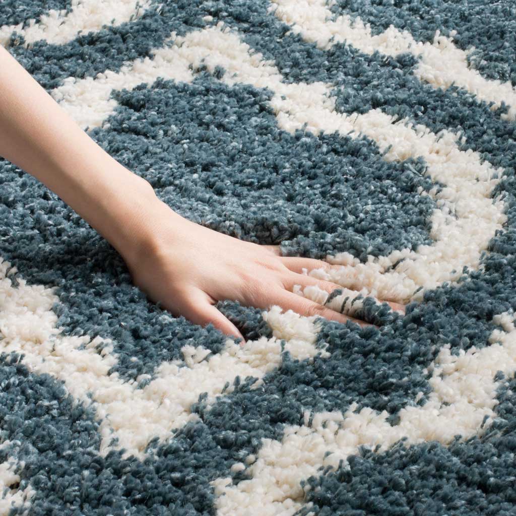 A hand presses into dense slate blue fibers beside ivory detailing