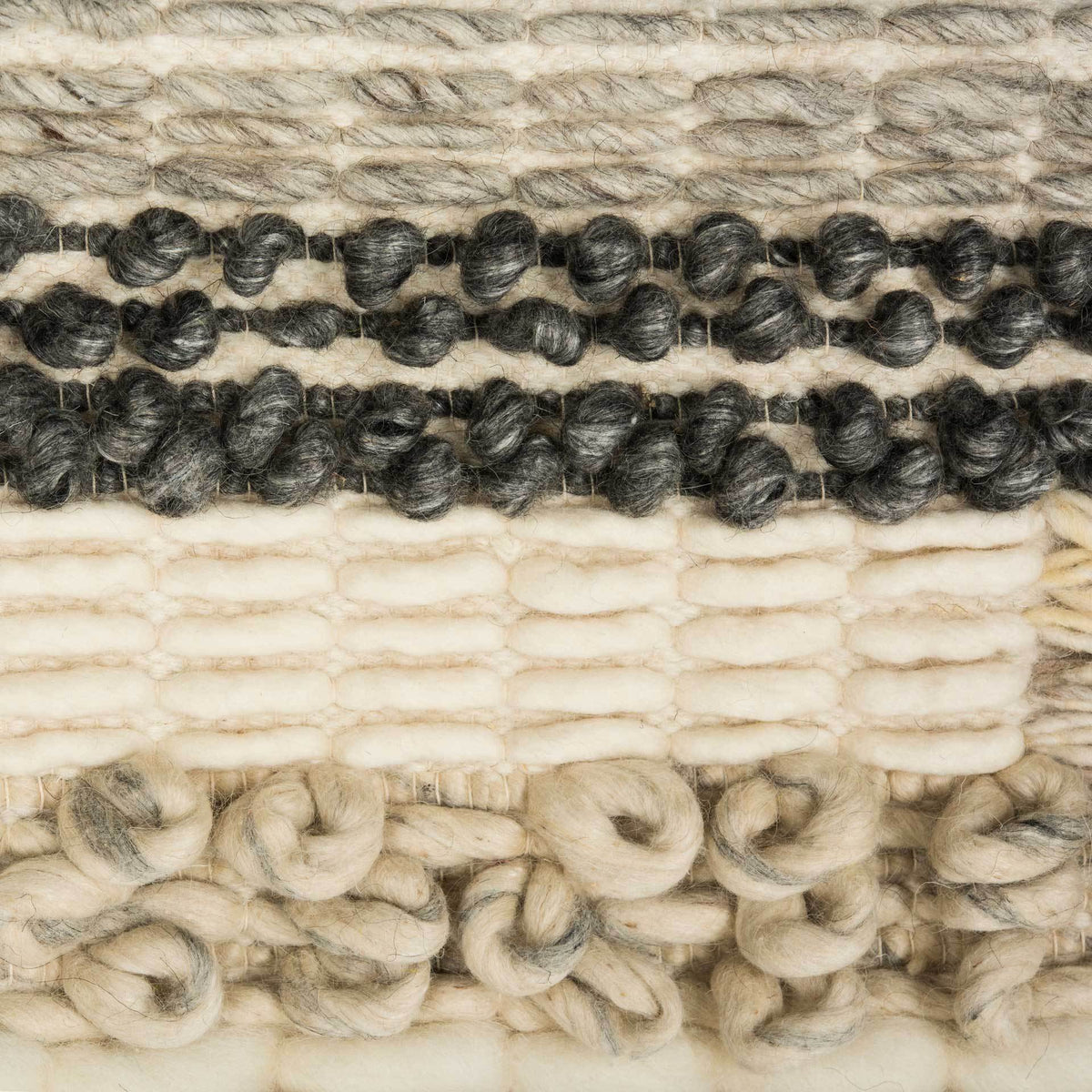 Dark charcoal bobbles and creamy raised loops punctuate the tapestry's varied natural weave.