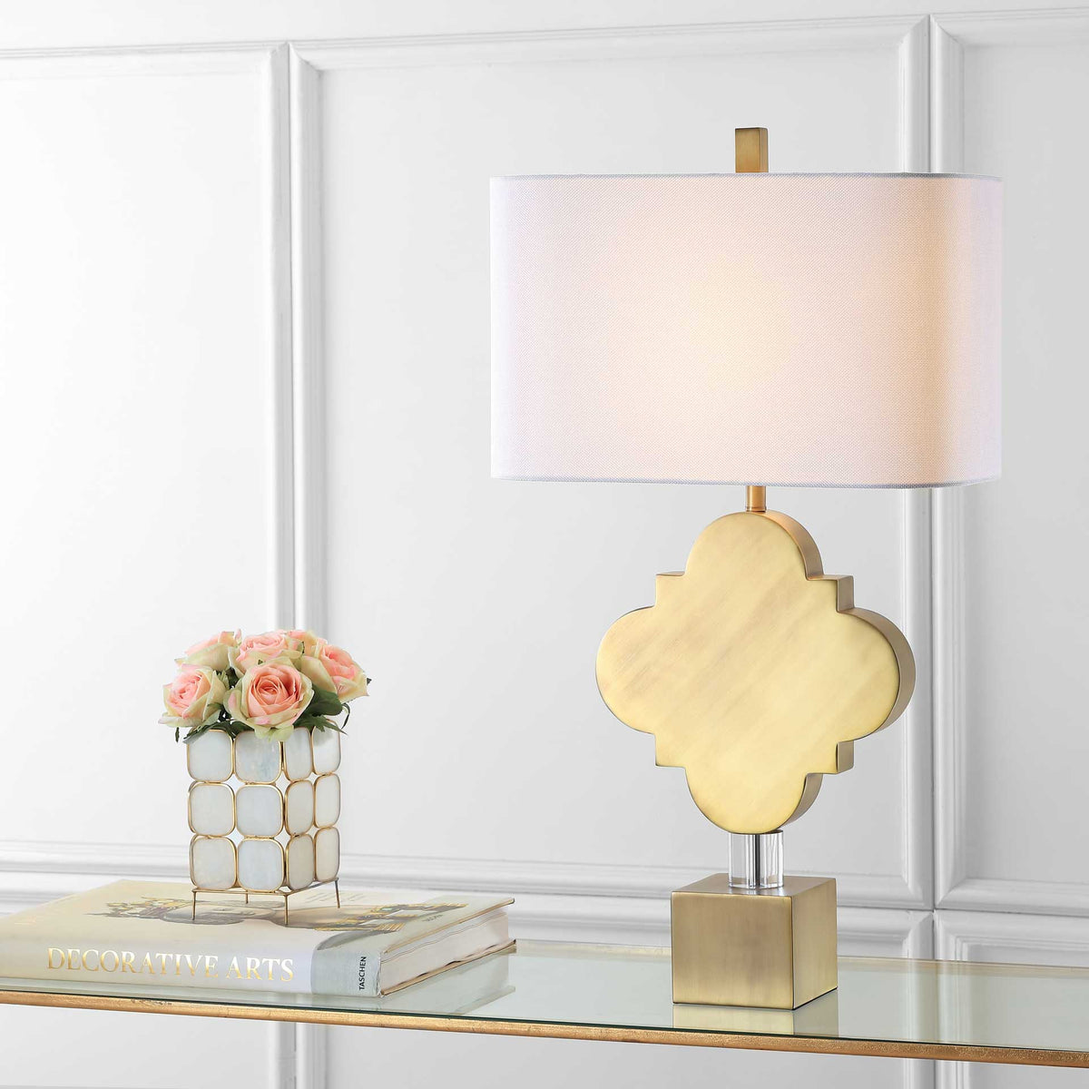 Warm light filters through the white shade above the gold quatrefoil and crystal stem