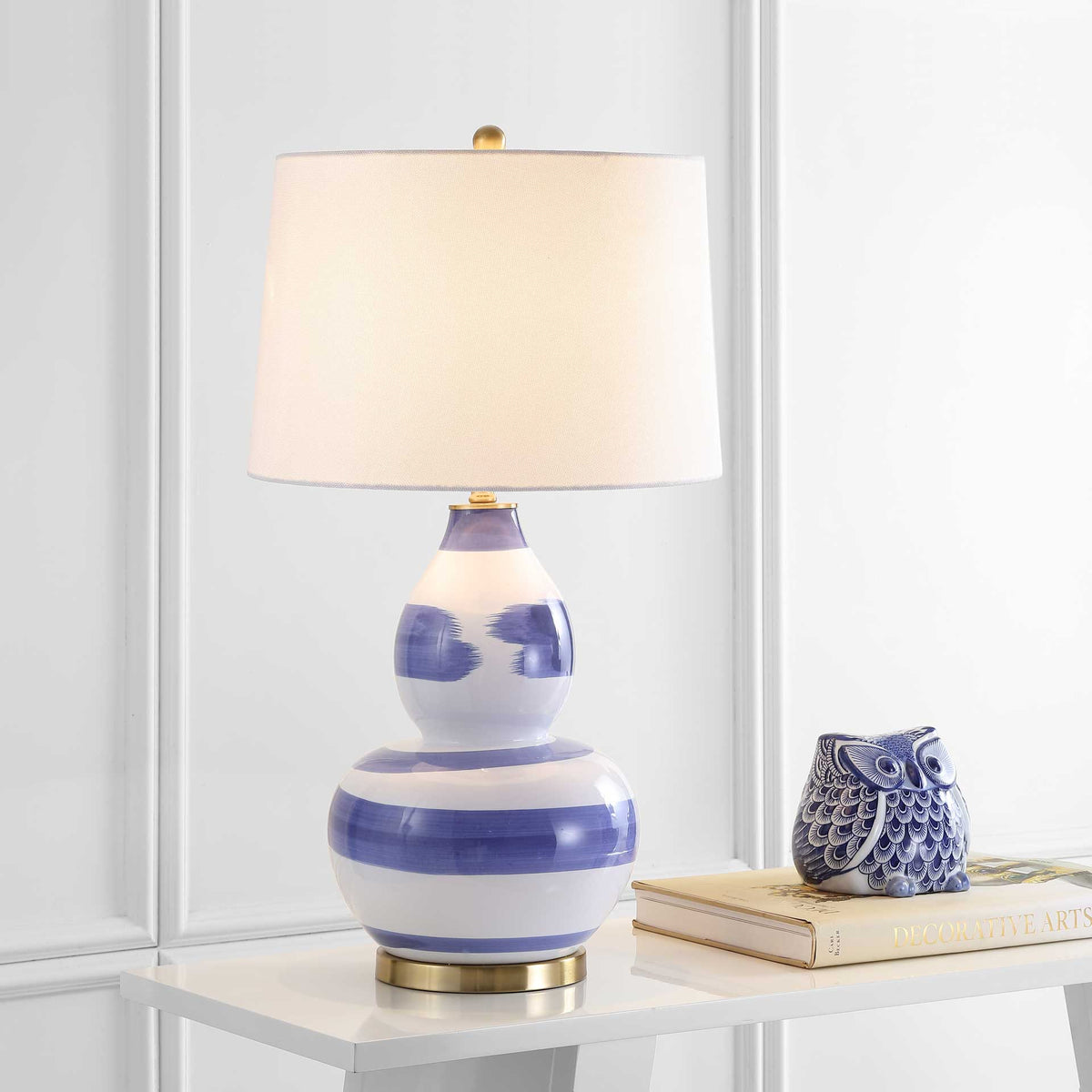 A softly glowing white shade tops a blue-striped ceramic base with a polished gold foot and finial.