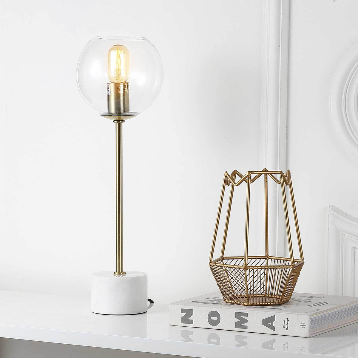 A warm bulb glows inside a clear globe, bringing inviting light to a slender gold lamp with a white marble base