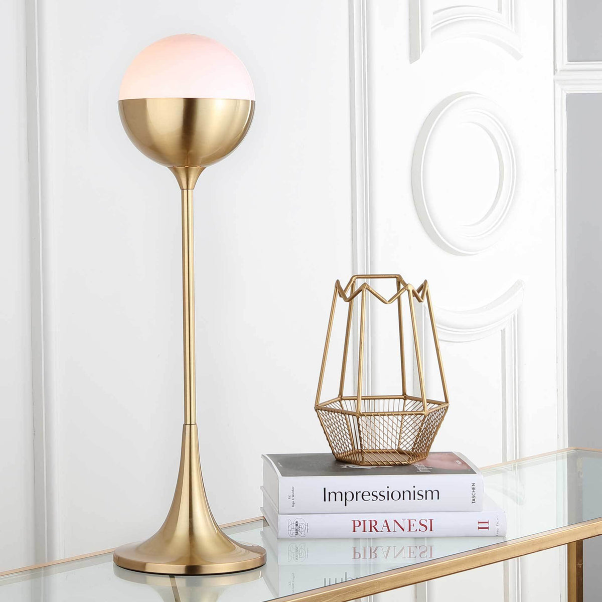 Warm light shines through the white dome shade atop a graceful gold pedestal