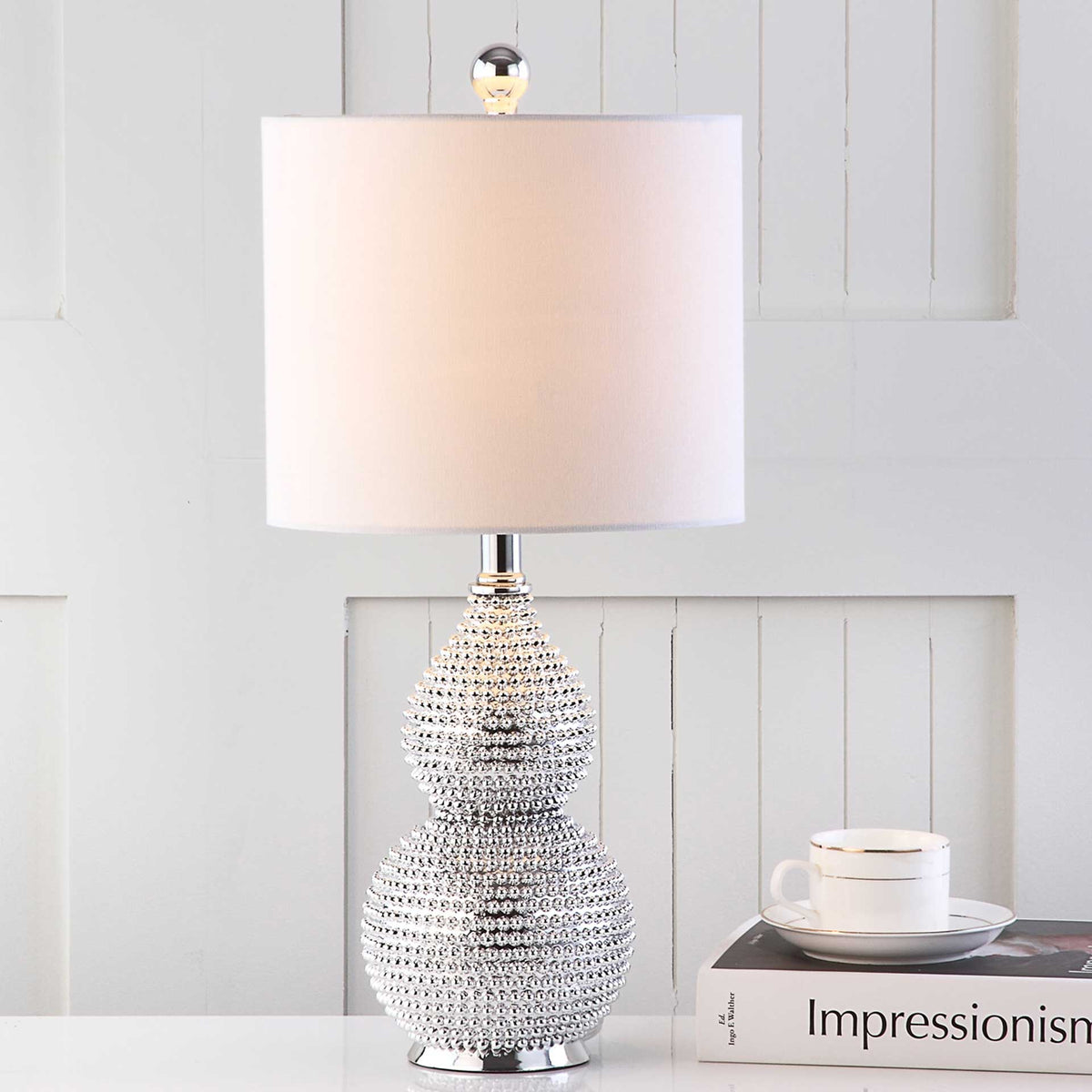A glowing white shade and reflective, beaded silver base add warmth and shine to a tabletop.