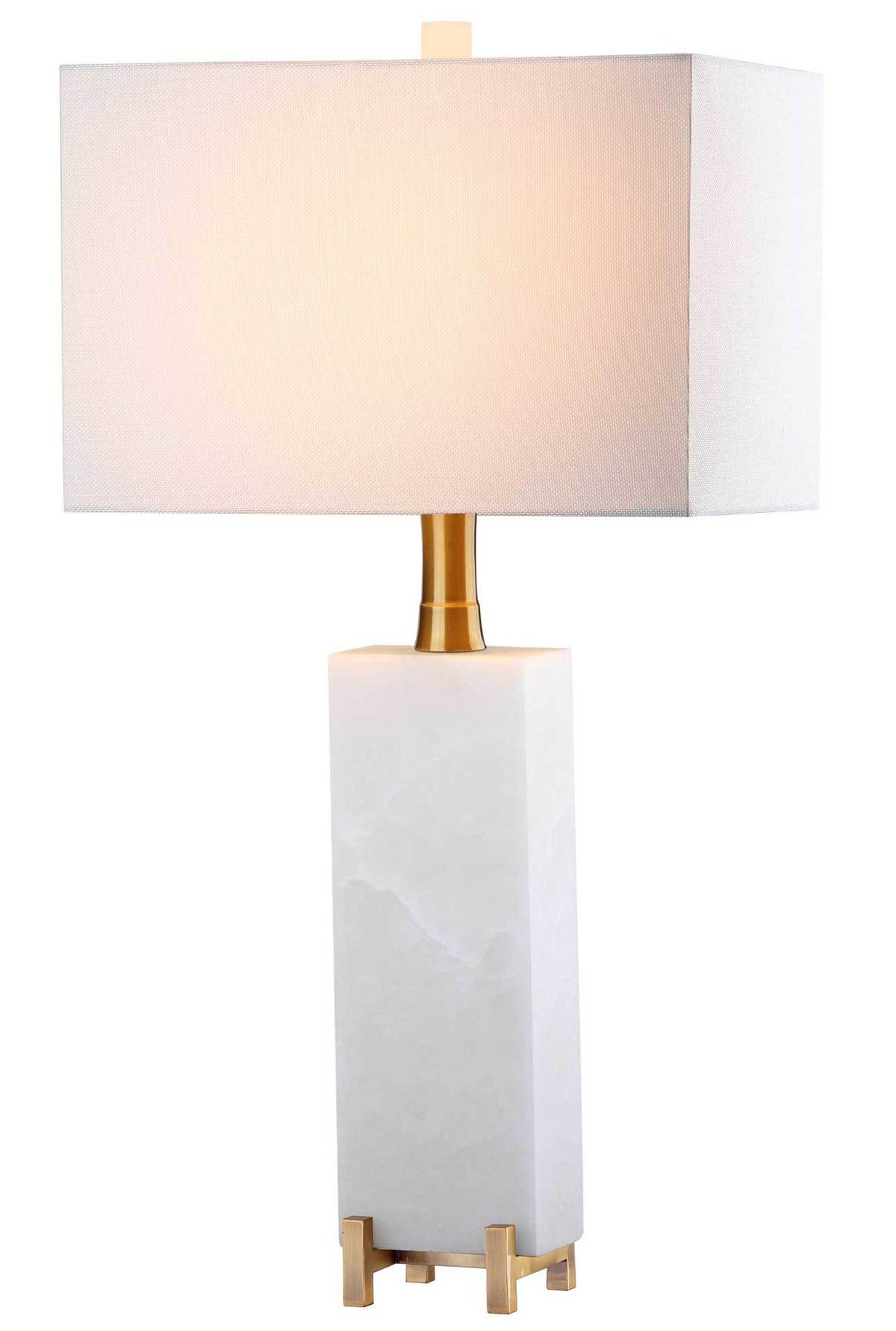 Warm light glows through the white fabric shade above an alabaster base with gold accents