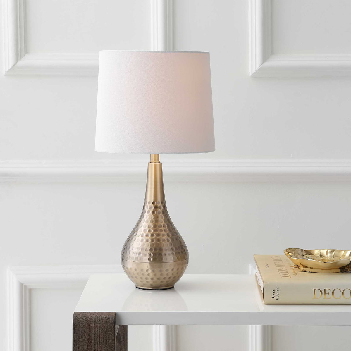 Soft illumination warms the white fabric shade above a rounded, hammered gold base