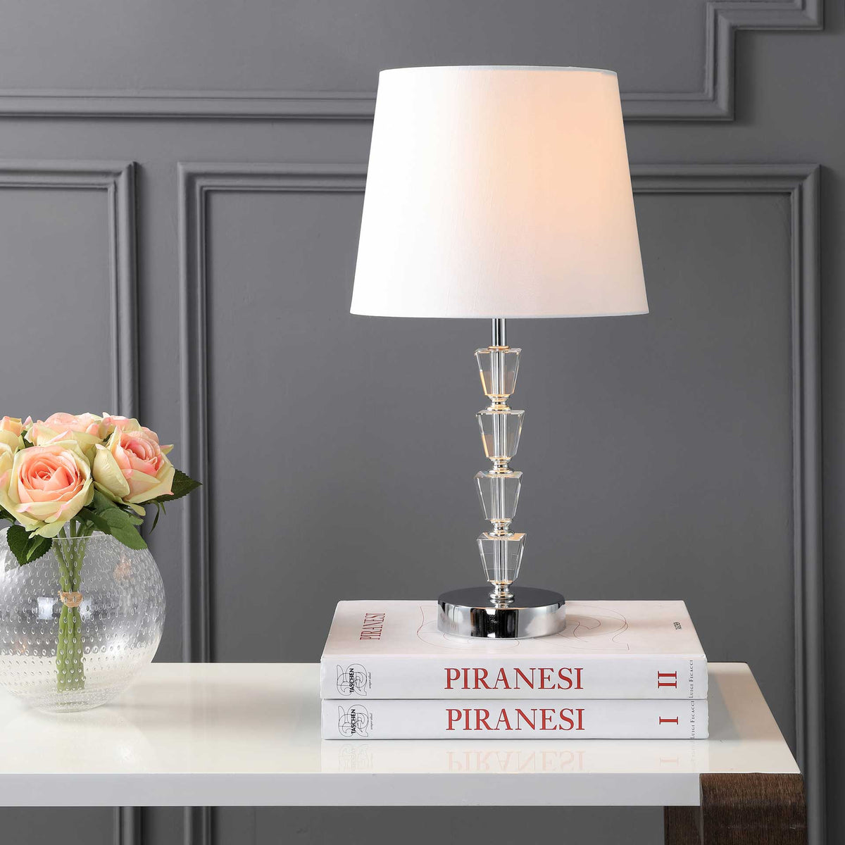 A softly glowing shade warms the stacked crystal accents and reflective chrome base