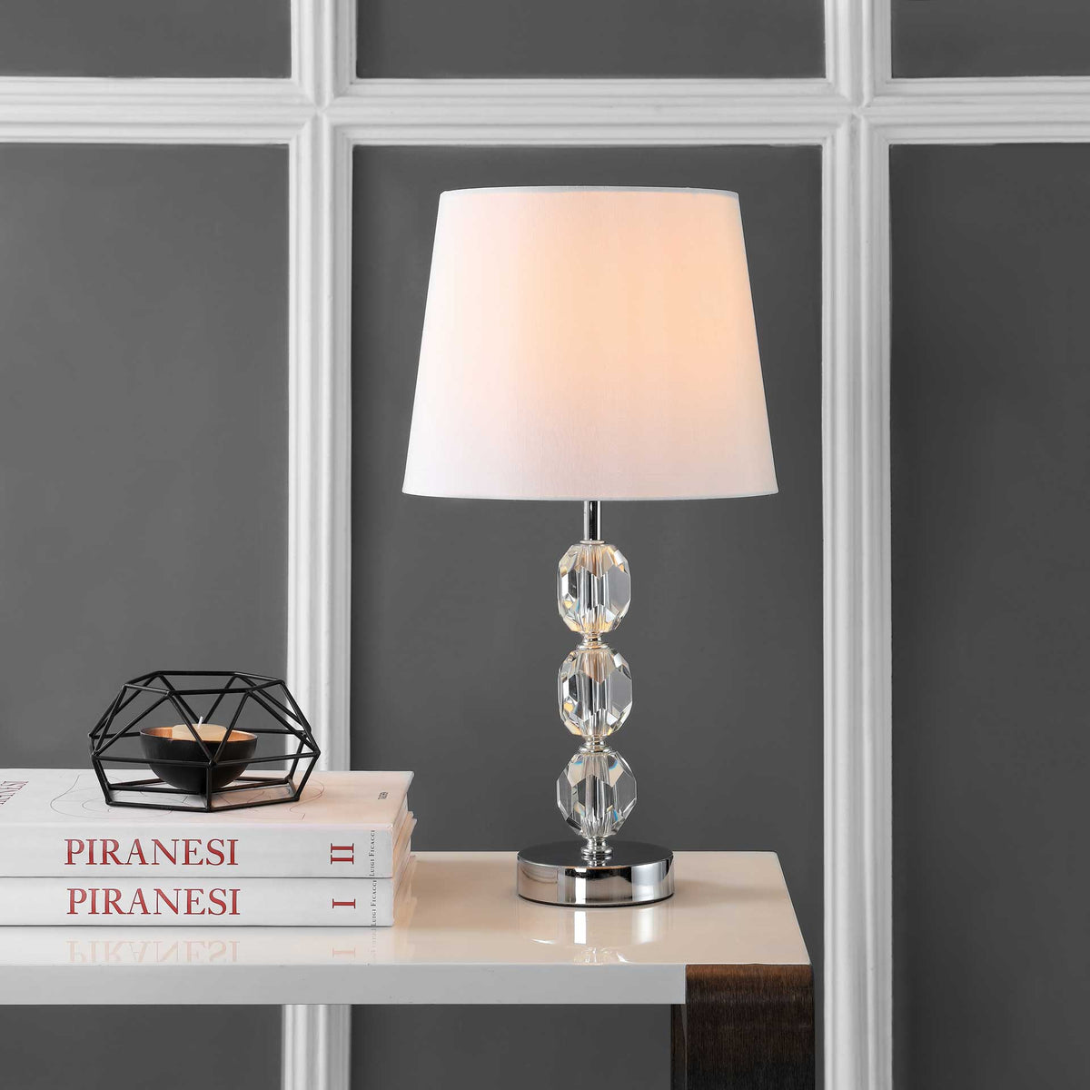 Warm light shines through a white shade above a trio of faceted crystals and a chrome base
