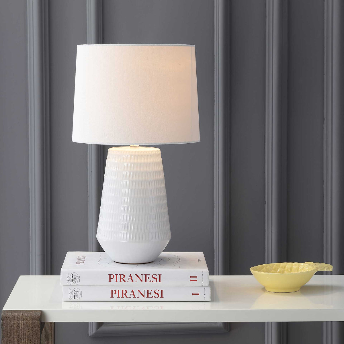 A gentle glow warms the white fabric shade and highlights the ceramic base's raised pattern.