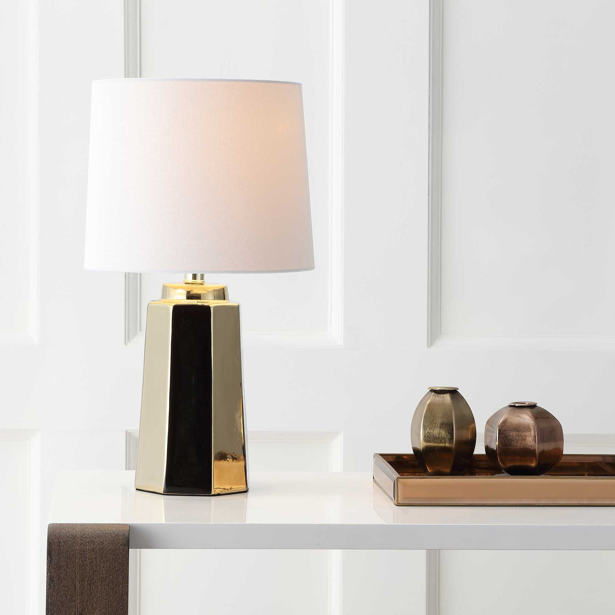 A softly glowing white shade adds warmth to a tapered gold ceramic base with a black accent