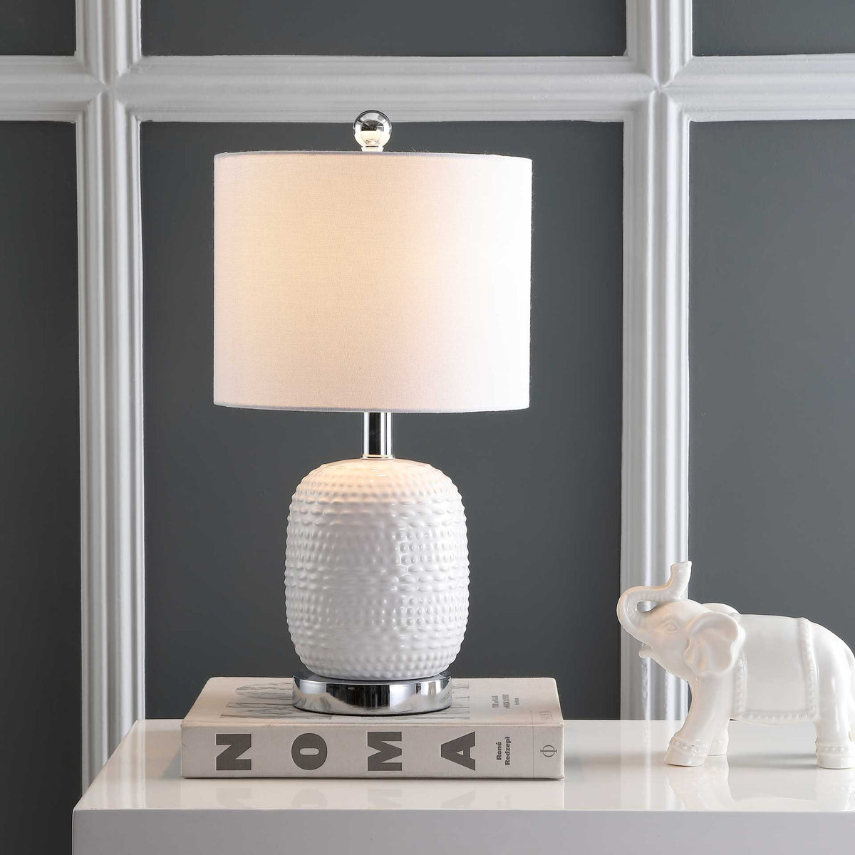 Warm light filters through the white drum shade, accenting the dimpled ceramic base and chrome trim