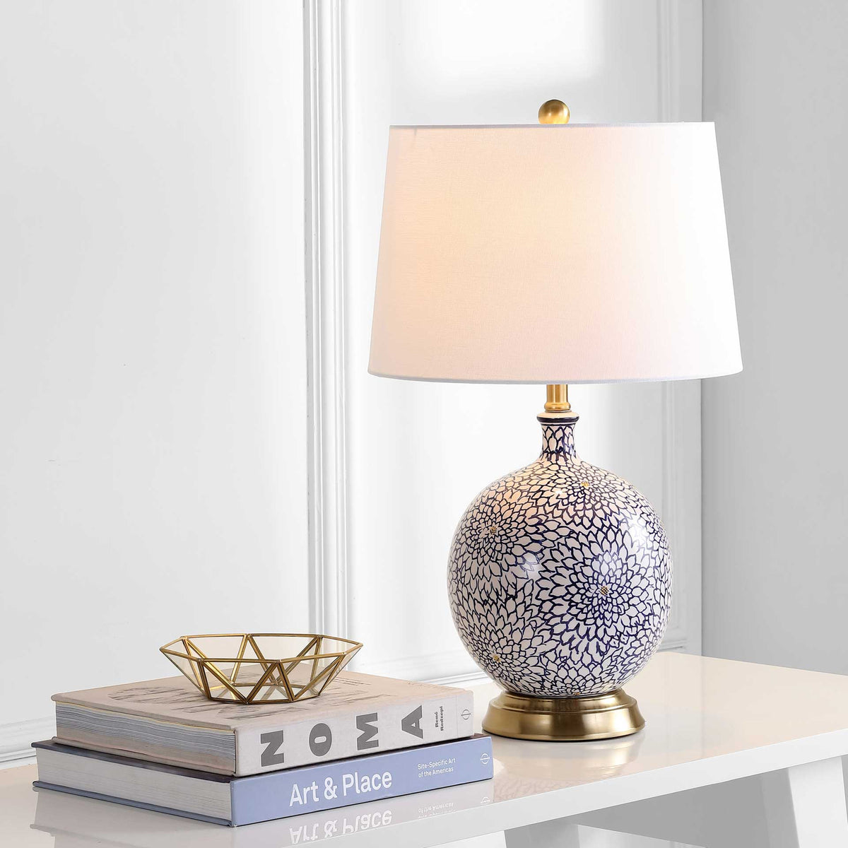 Warm light glows through the white shade above a blue-and-white floral ceramic base and brass-toned foot