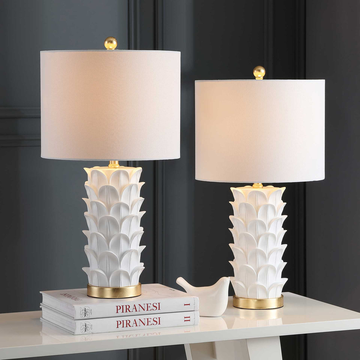 Warm light fills two white drum shades above layered leaf bases and gleaming gold trim.