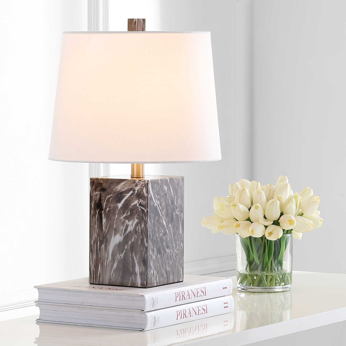 Warm light glows through the white shade above a dark brown block base with pale veining