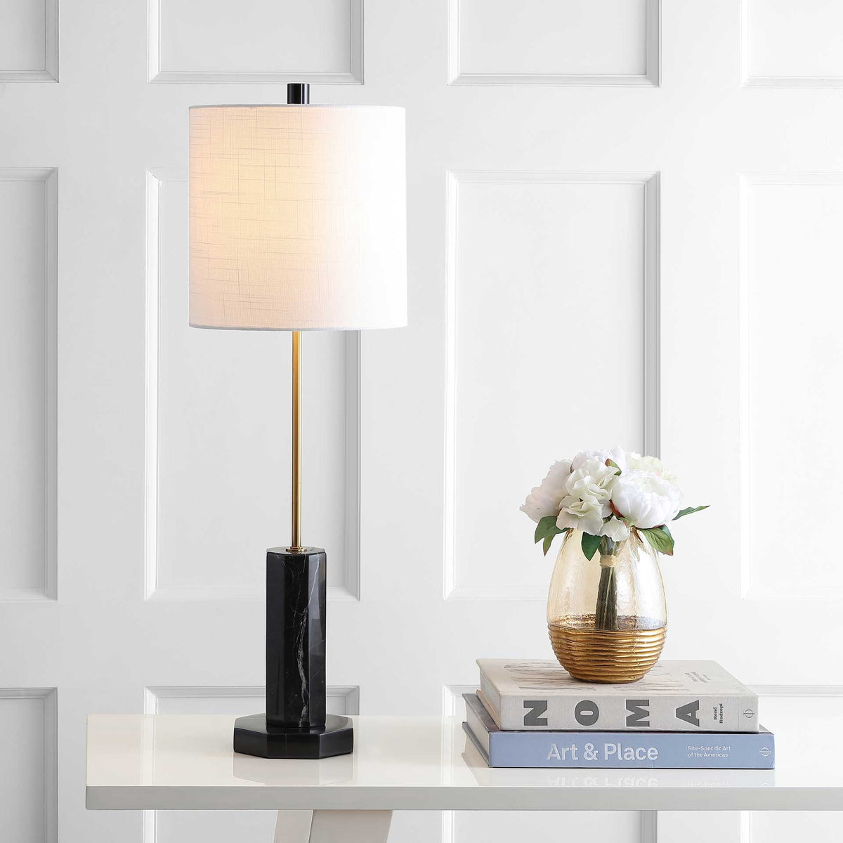 A softly glowing white drum shade lends warmth to the gold-toned stem and black marble base.
