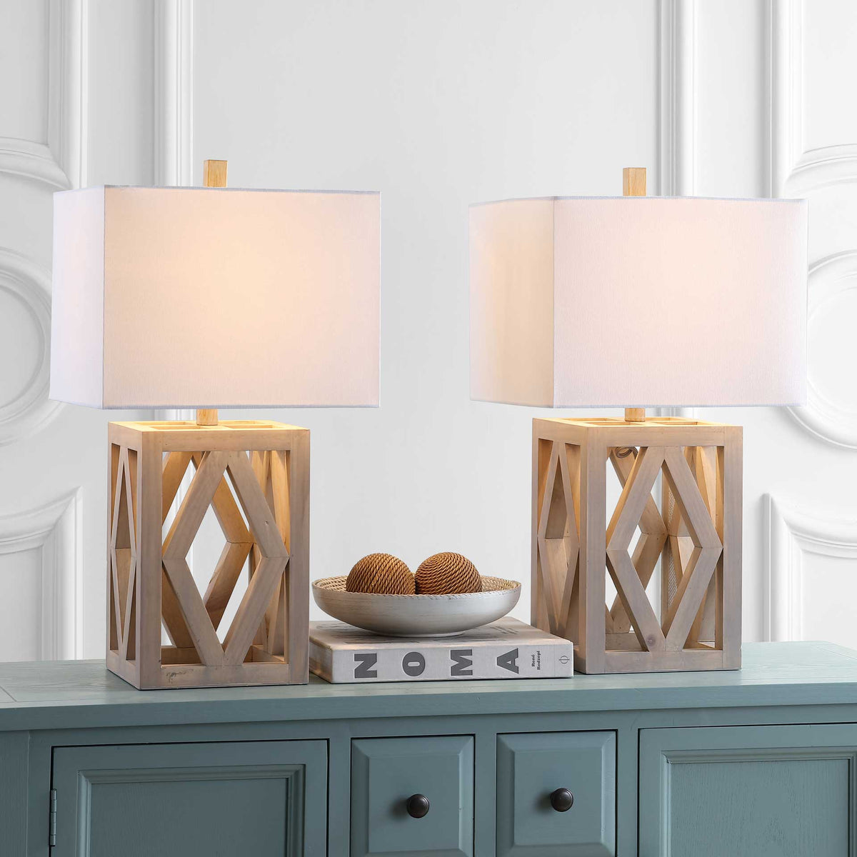 Two illuminated lamps pair glowing white shades with open geometric wood bases