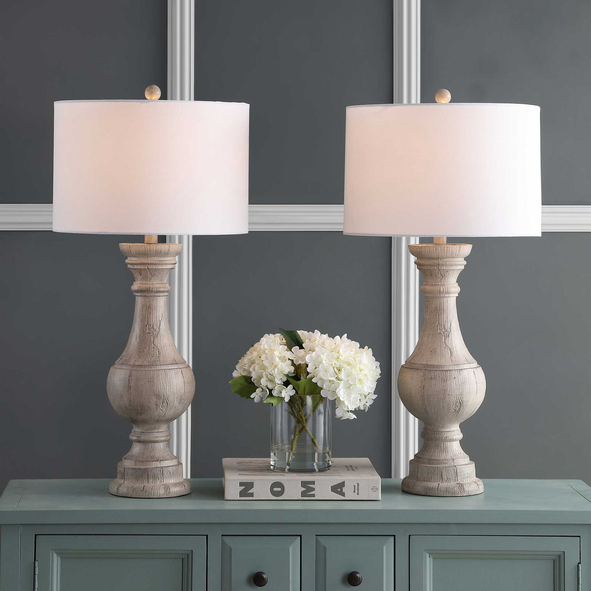 A pair of whitewashed urn lamps casts a warm glow through white fabric drum shades.