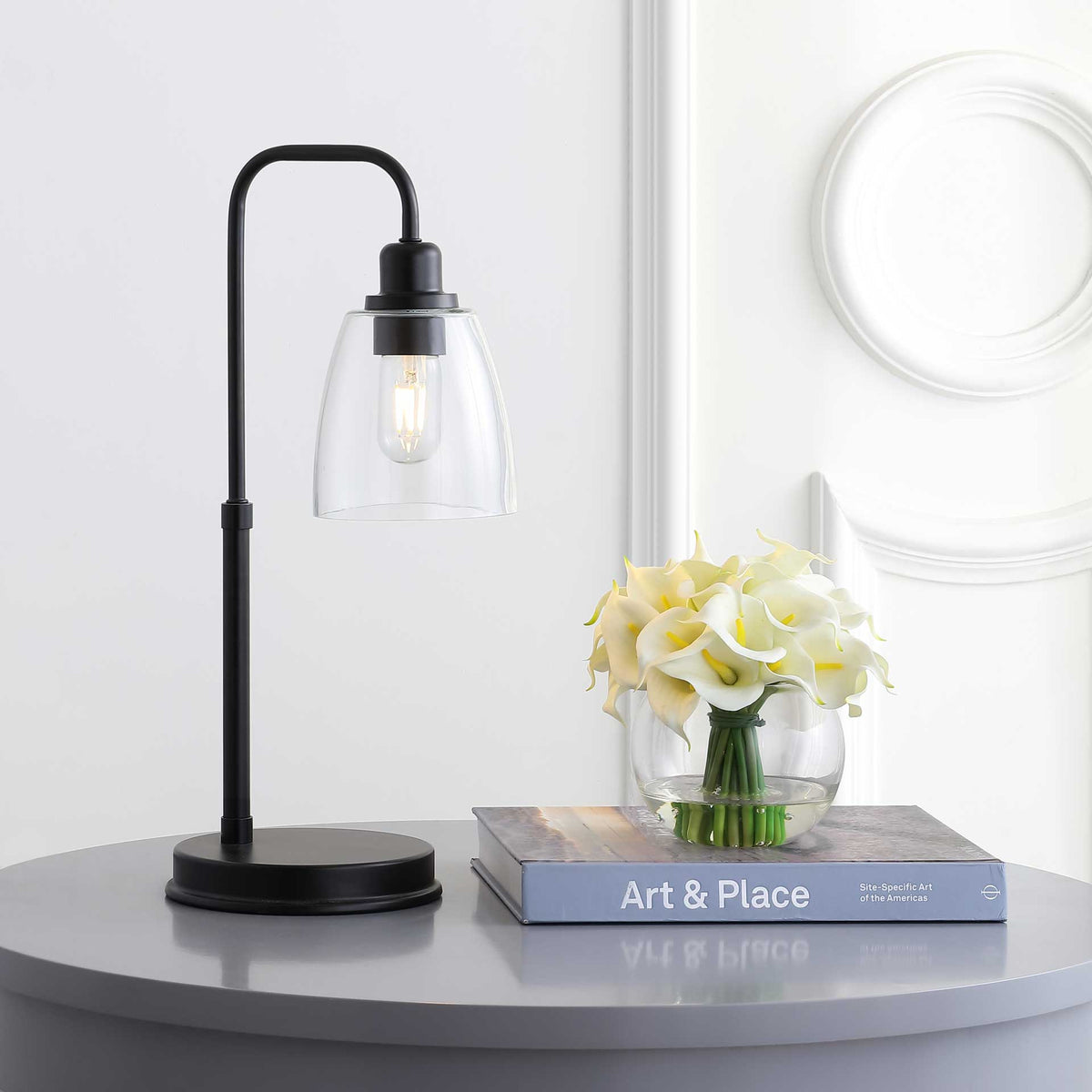 Warm light shines through the clear glass shade of this curved black task lamp.