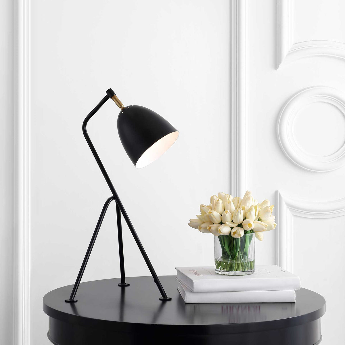 Warm downlight shines from the black bell shade above a slim tripod base