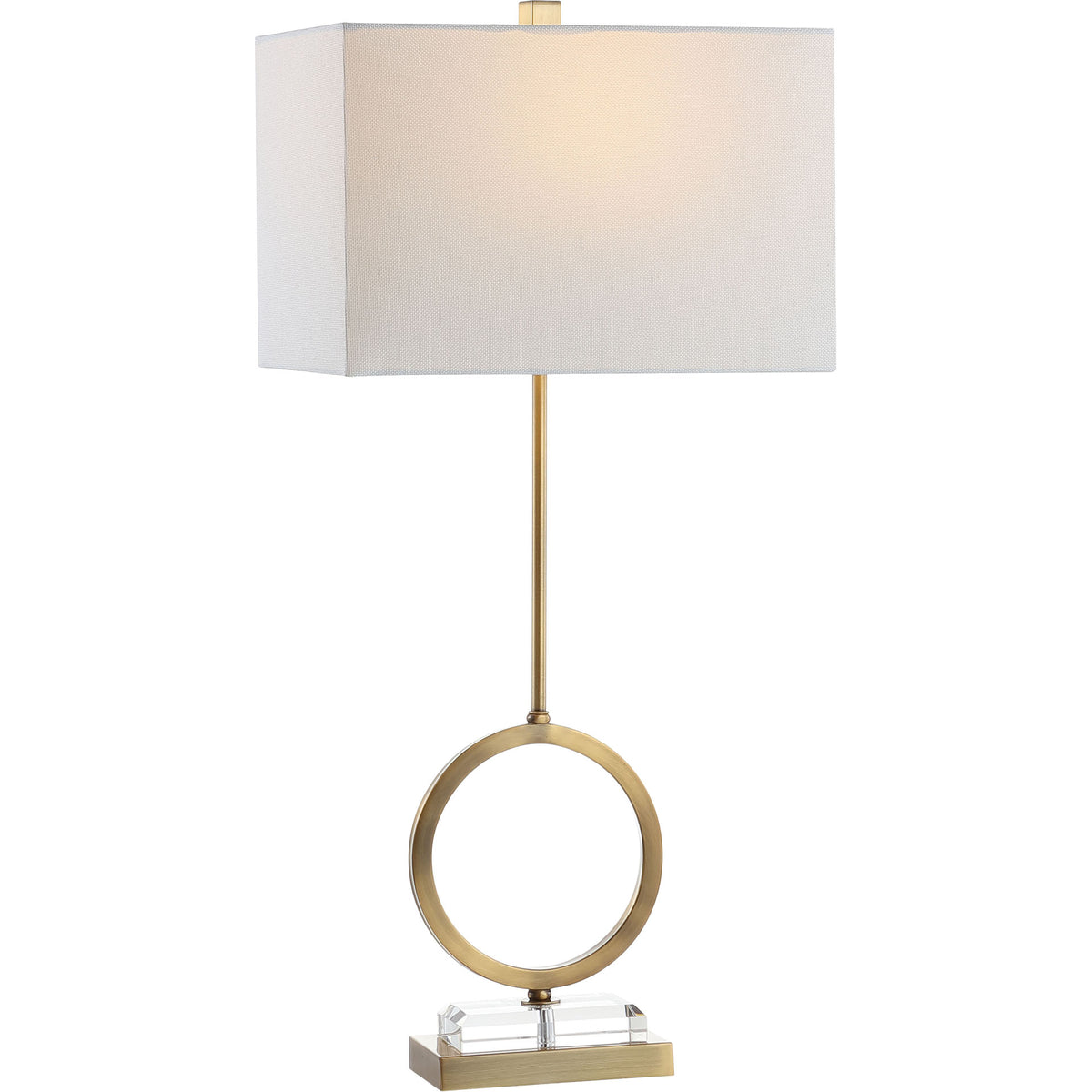 Warm light glows through a white shade above a sculptural brass circle and clear crystal base