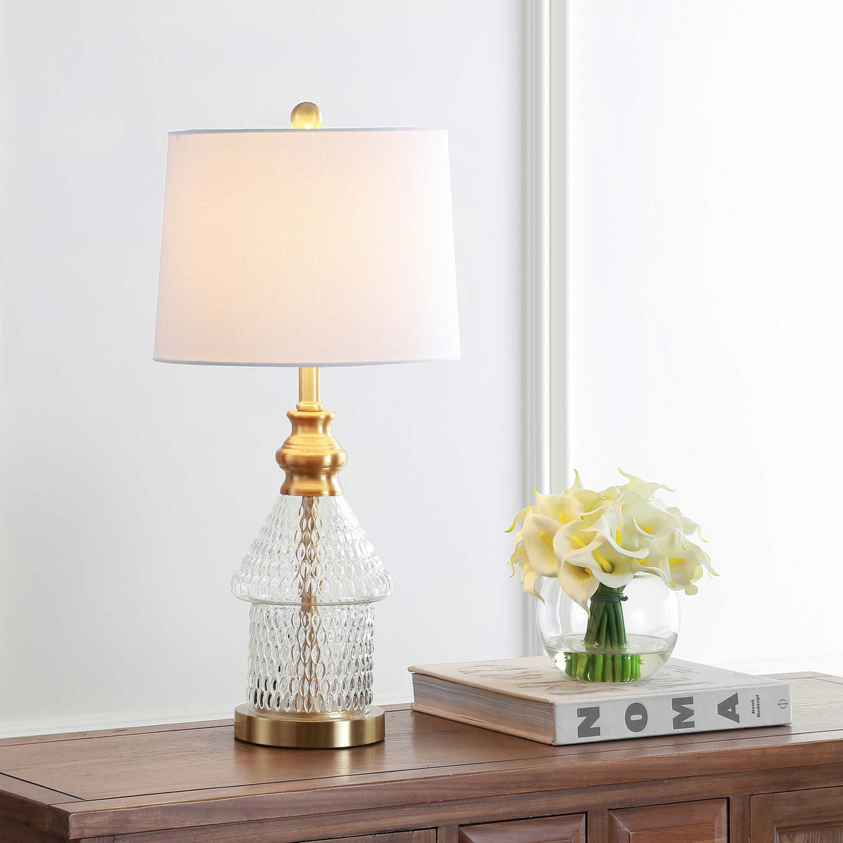 Soft light shines through the white shade above a sculpted glass base with golden accents