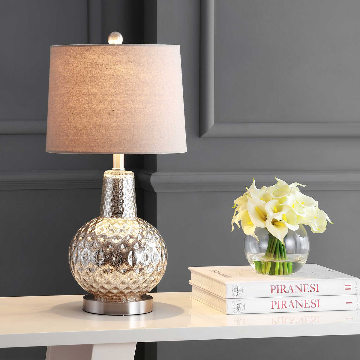 A warm glow brings out the patterned mercury-glass base beneath a light gray fabric shade.