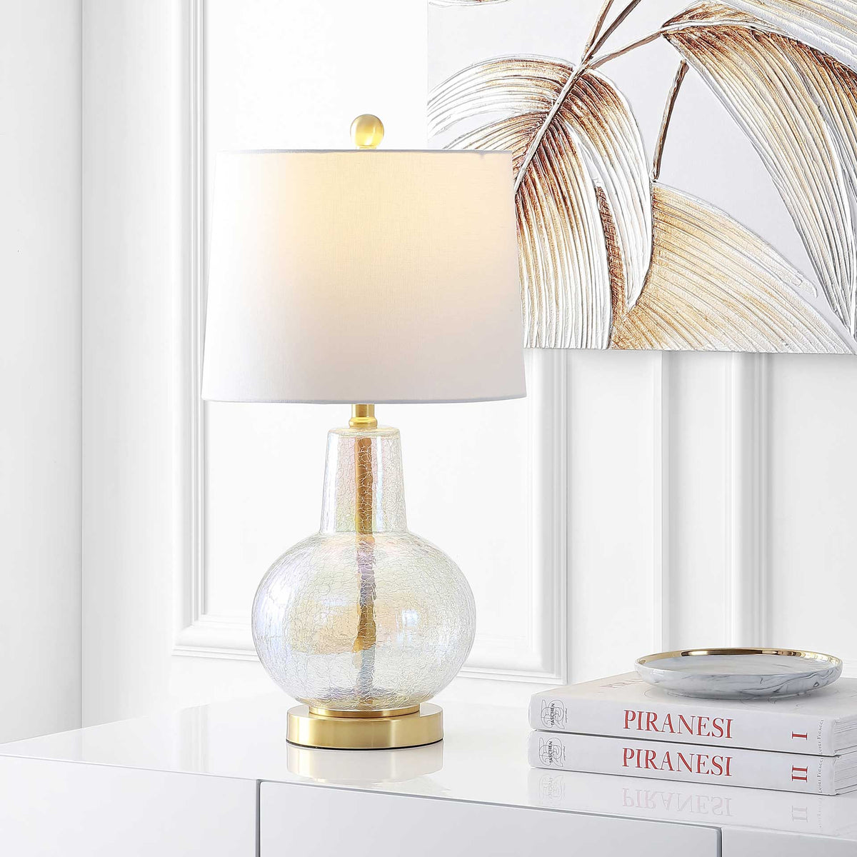 Warm light fills the white shade above an iridescent glass base and gleaming brass-tone foot.