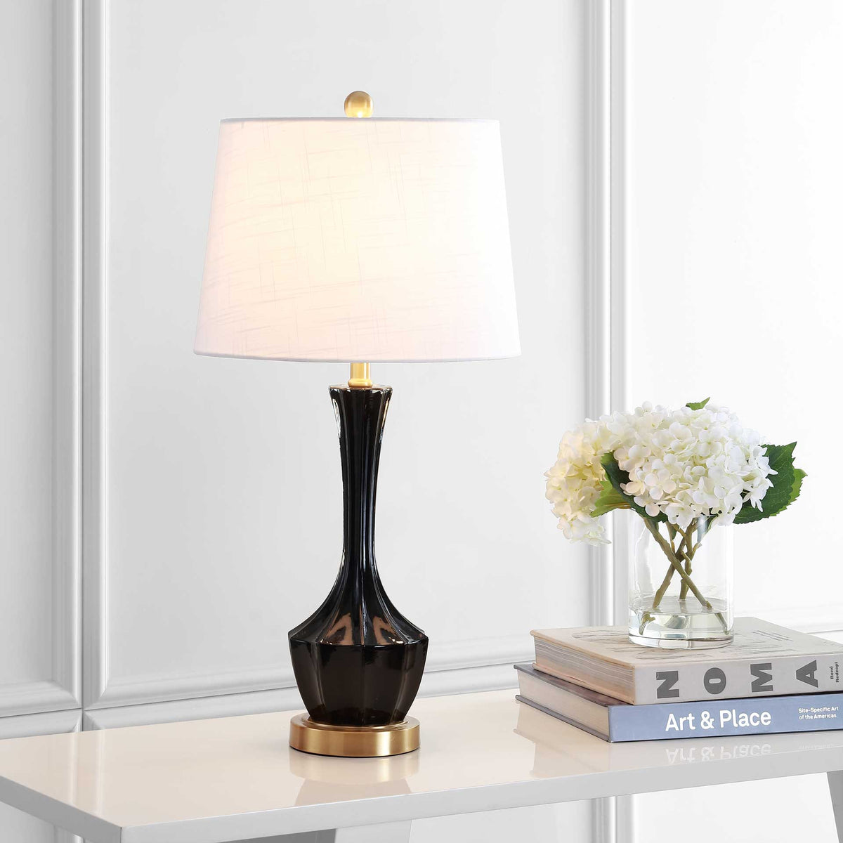 A warm glow illuminates the white shade atop a sleek black glass lamp with gold-tone accents
