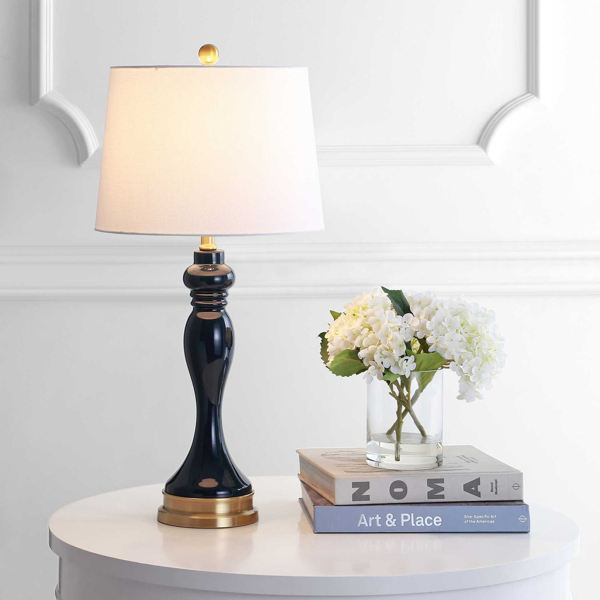 Warm light glows through a white fabric shade above a glossy navy base with gold trim