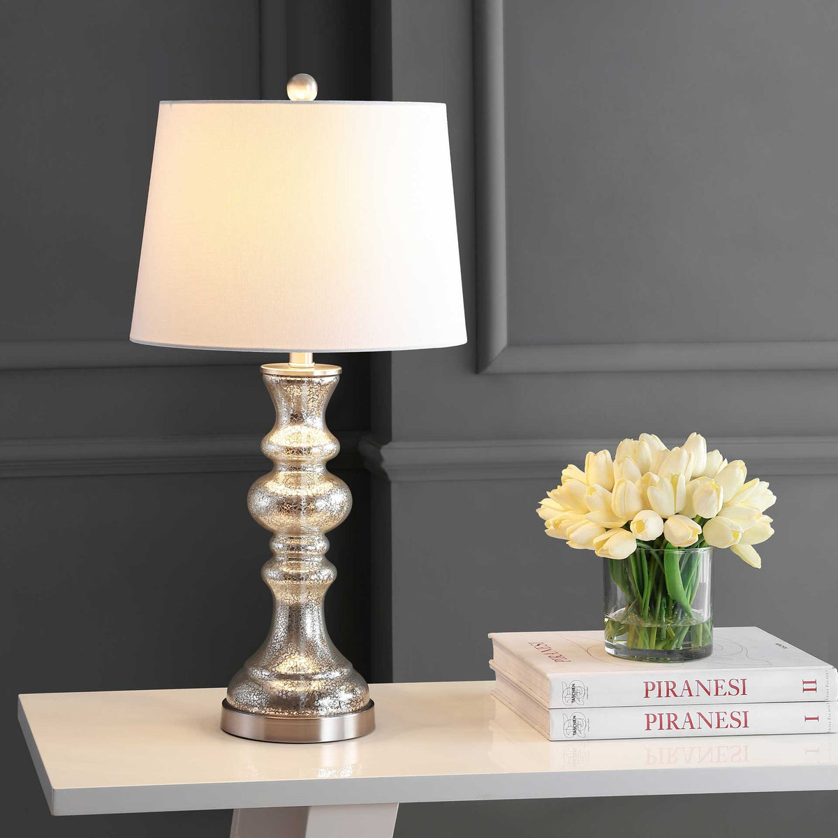 Warm light shines through the white shade, highlighting the reflective mercury-glass base.