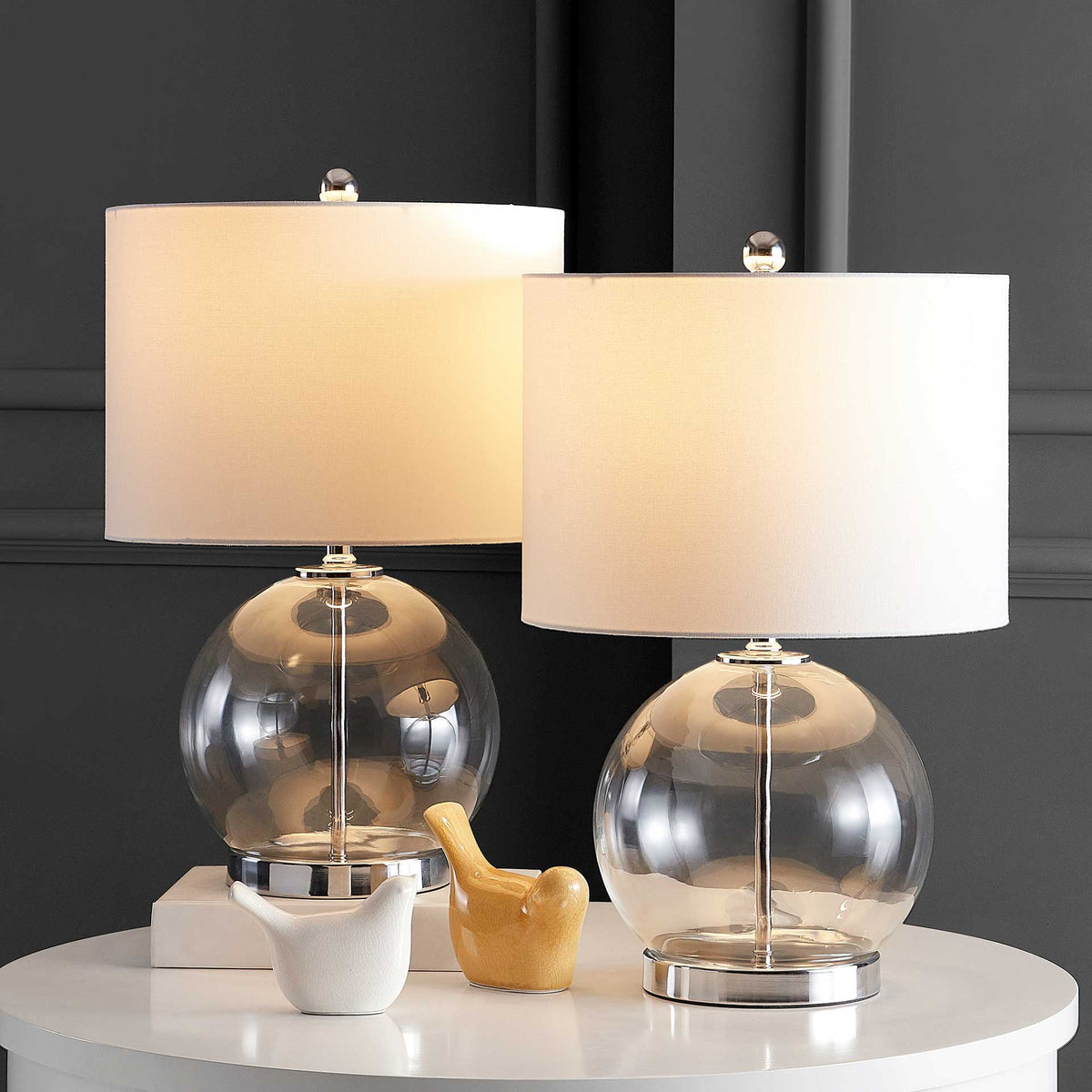 A pair of clear glass globe lamps casts warm light over a tabletop with gleaming chrome accents