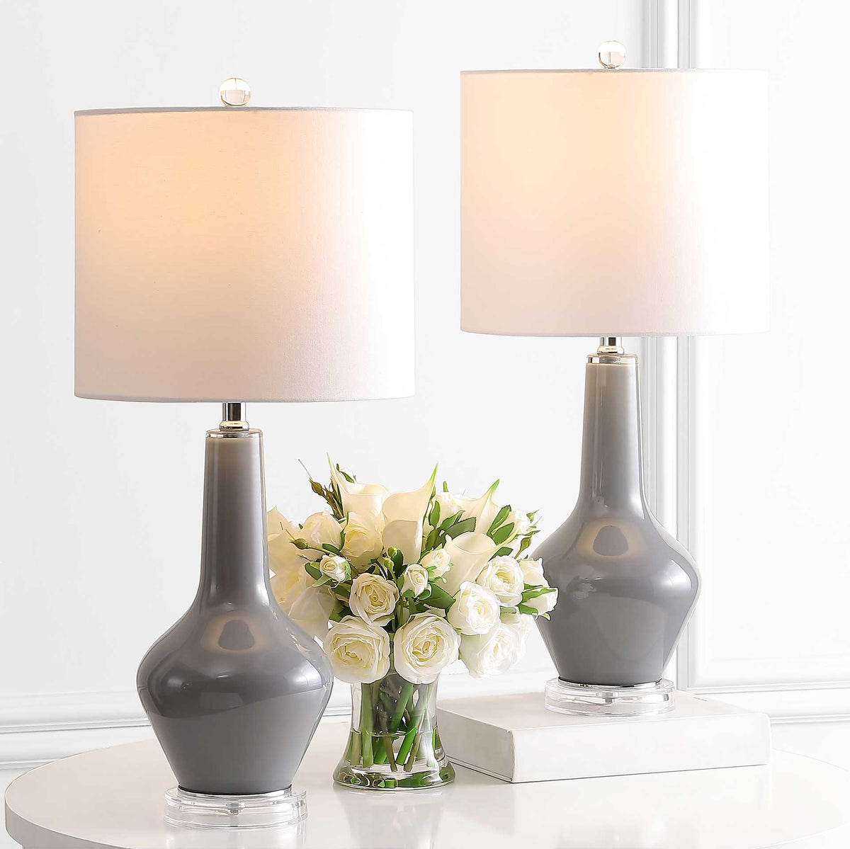 Two gray glass lamps cast a gentle glow from their white drum shades above clear feet