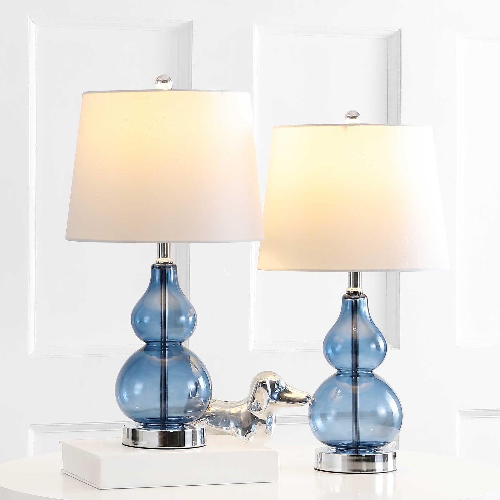 Two blue glass lamps cast a warm glow through white shades above gleaming chrome bases. || TBL4222B-SET2 || front_multi_on_room