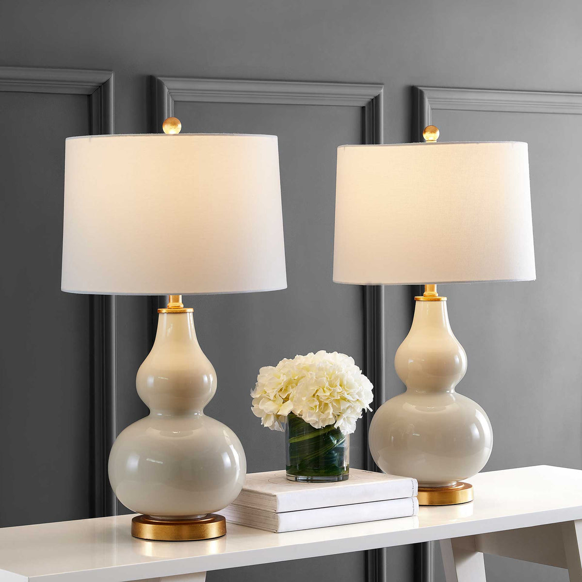 Matching cream glass lamps illuminate a white console with warm light and softly glowing fabric shades.
