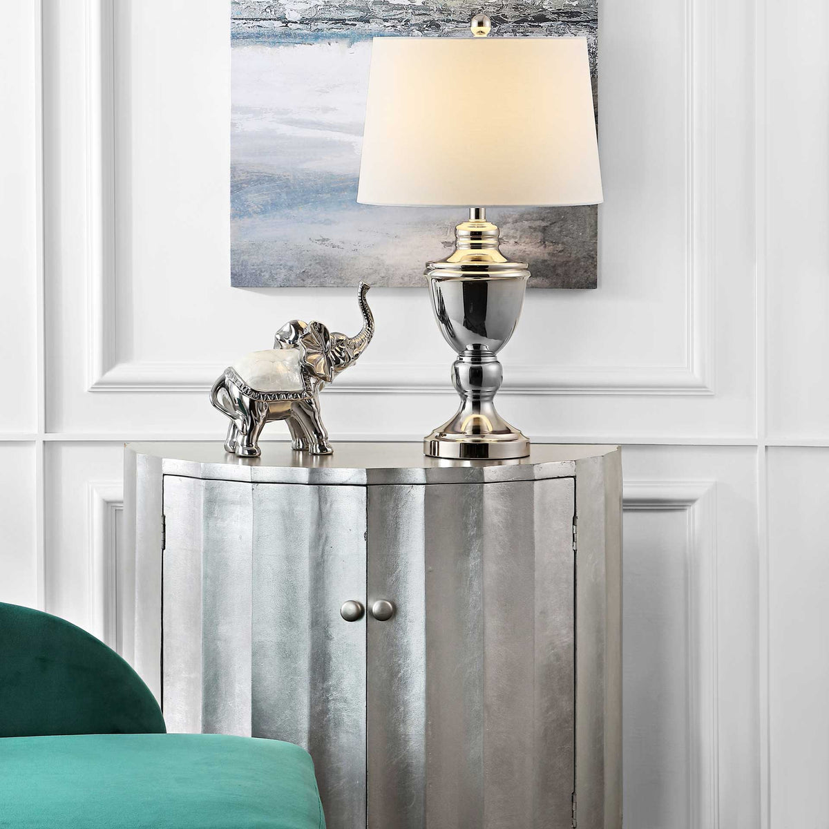 A glowing white shade crowns a polished nickel base atop a silver cabinet