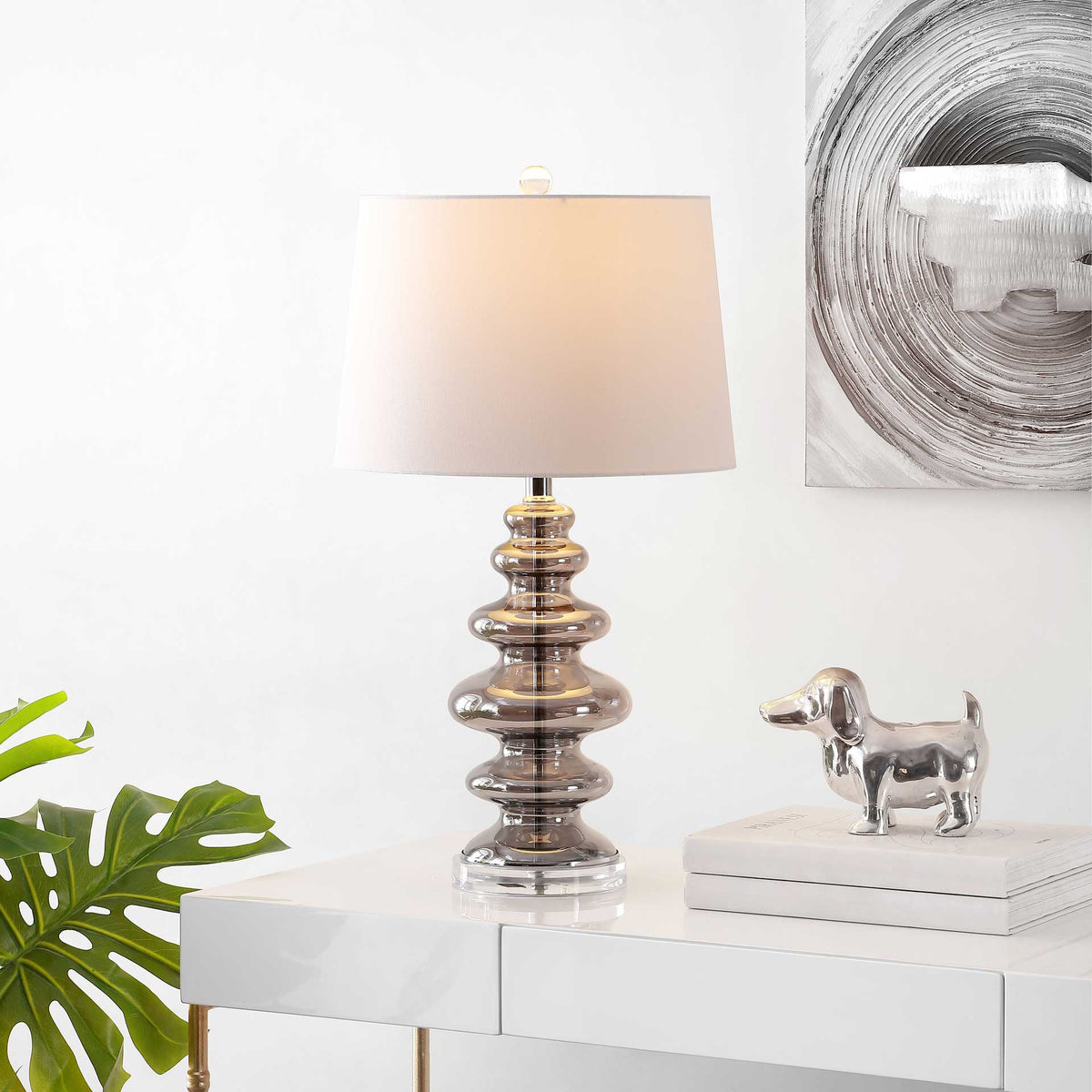 Warm light glows through the white shade above a sculpted glass base on a console.